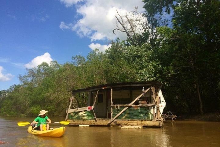 A kayak guest passes a broken down house boat on a honey island kayak swamp tour