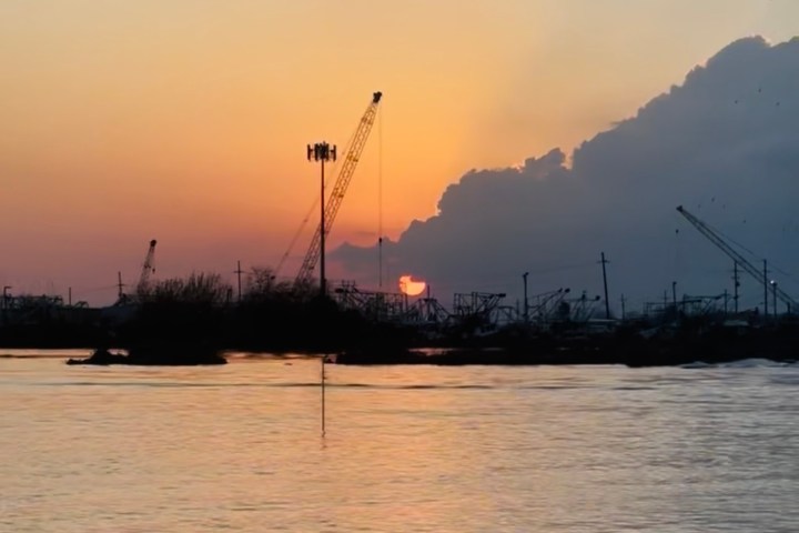 Sunset over water with cranes silhouetted against colorful sky.